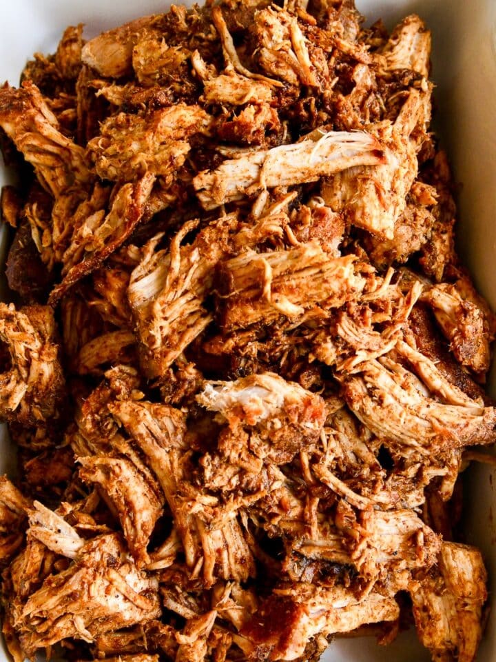 A white casserole dish with oven roasted pulled pork shredded and ready to eat in tacos or a recipe for dinner.