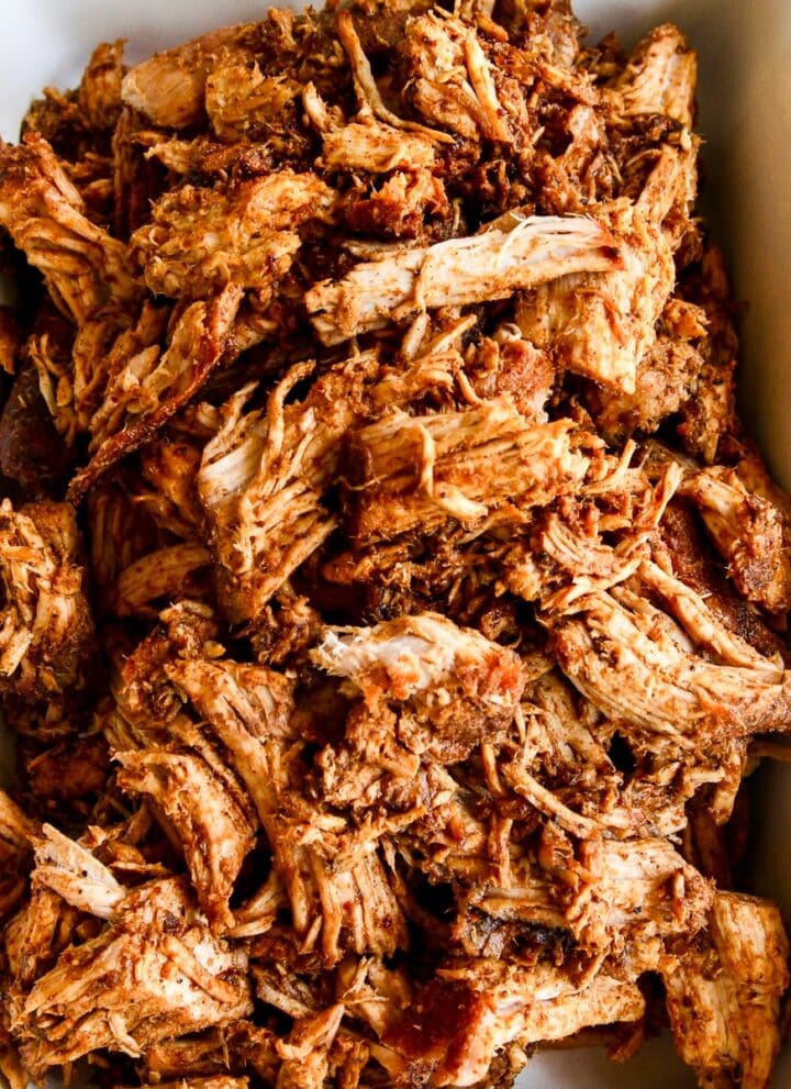 A white casserole dish with oven roasted pulled pork shredded and ready to eat in tacos or a recipe for dinner.