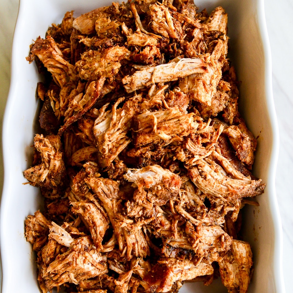 A white casserole dish with oven roasted pulled pork shredded and ready to eat in tacos or a recipe for dinner.