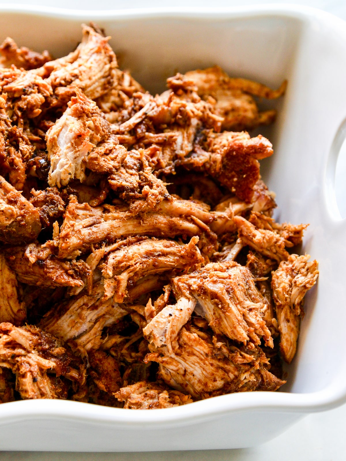 Pieces of pulled pork in a white casserole dish ready for dinner.