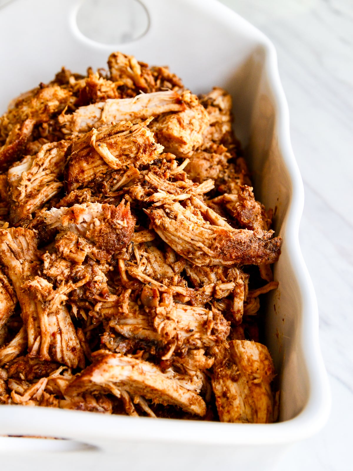 A white casserole dish with roasted pulled pork just out of the oven and seasoned with bbq rub.
