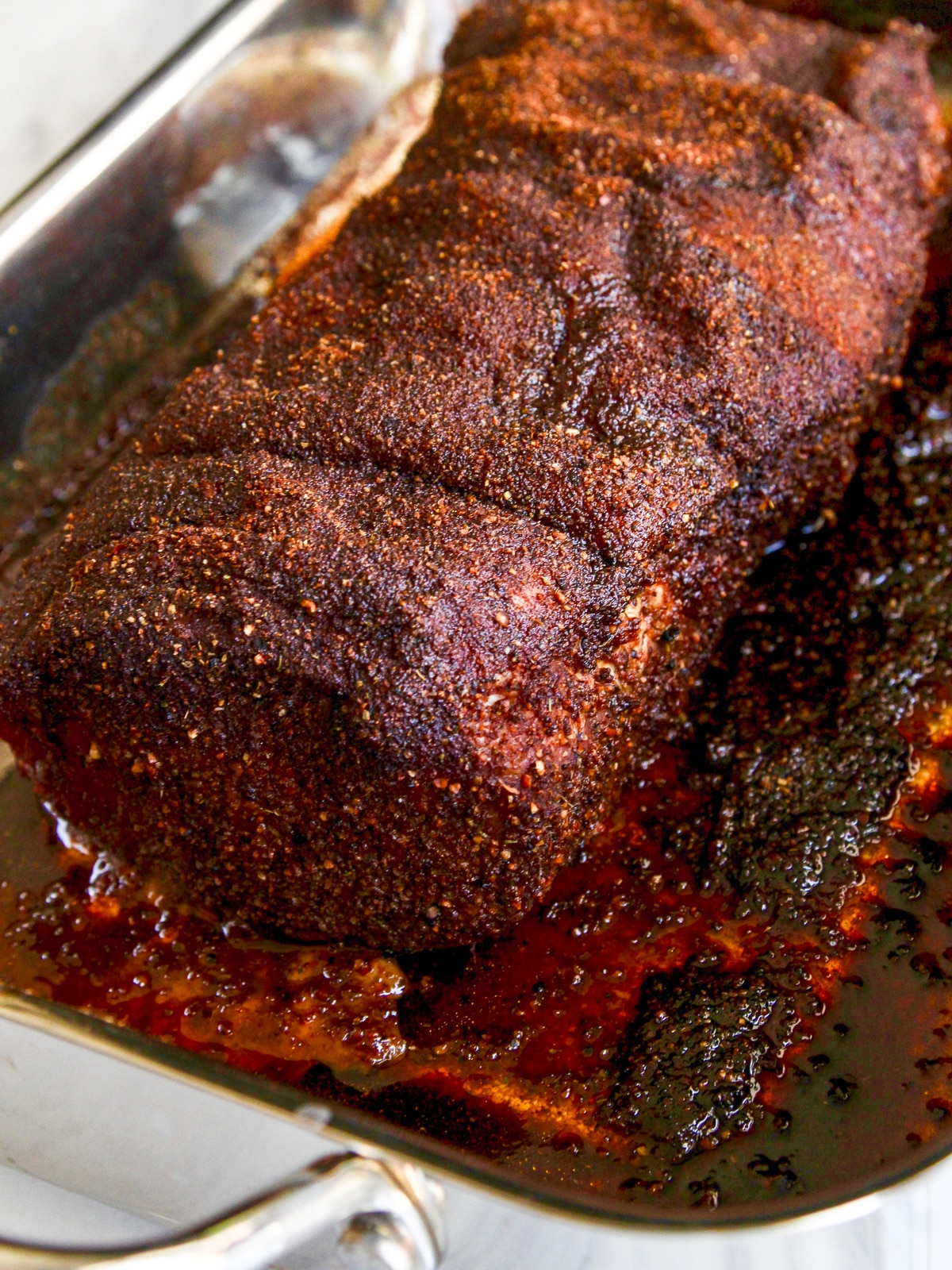 A fully cooked pork loin just out of the oven in a metal roasting pan covered with bbq rub, and ready to shred into pulled pork.