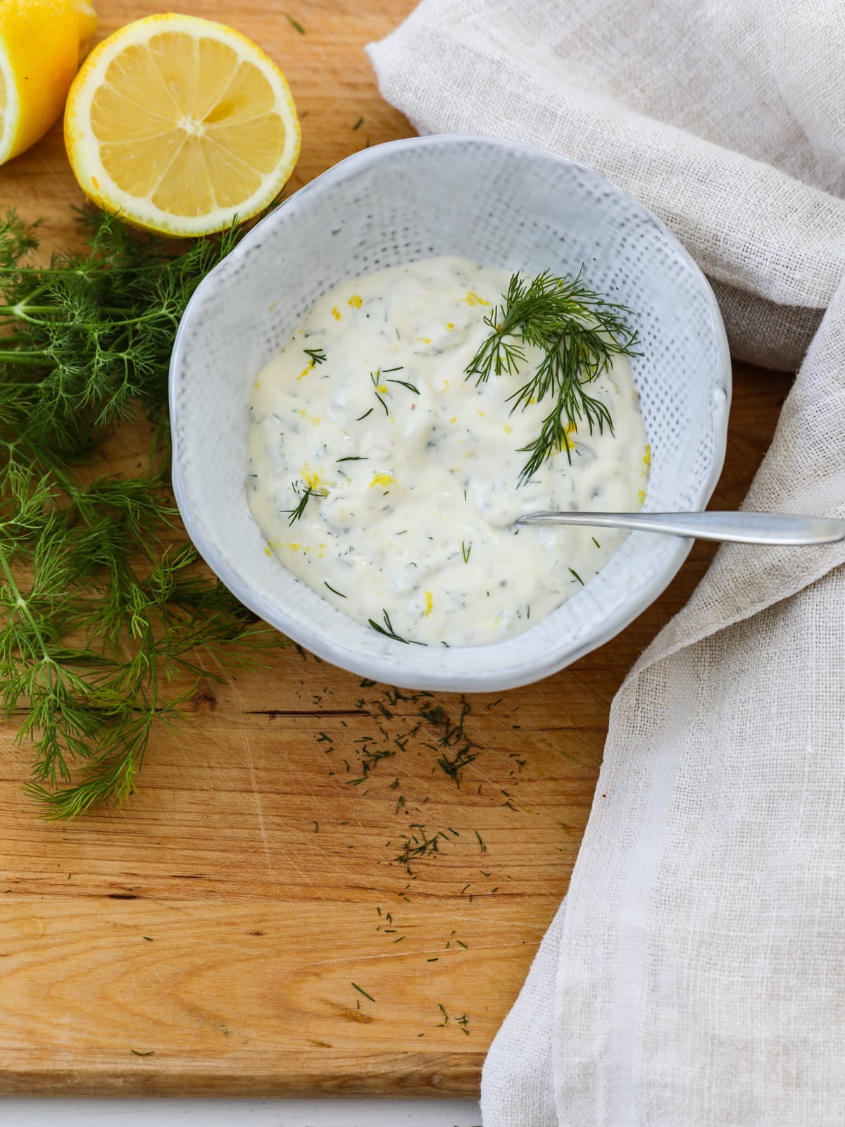 A small silver spoon in a white bowl of seafood sauce garnished with lemon and dill.