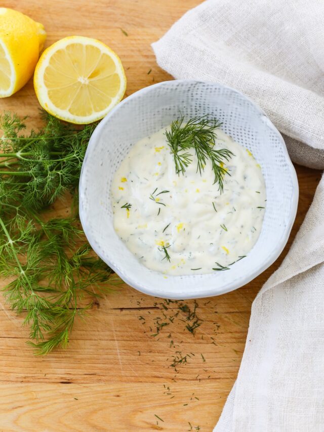 Looking down into a white ceramic bowl of seafood sauce garnished with fresh dill.