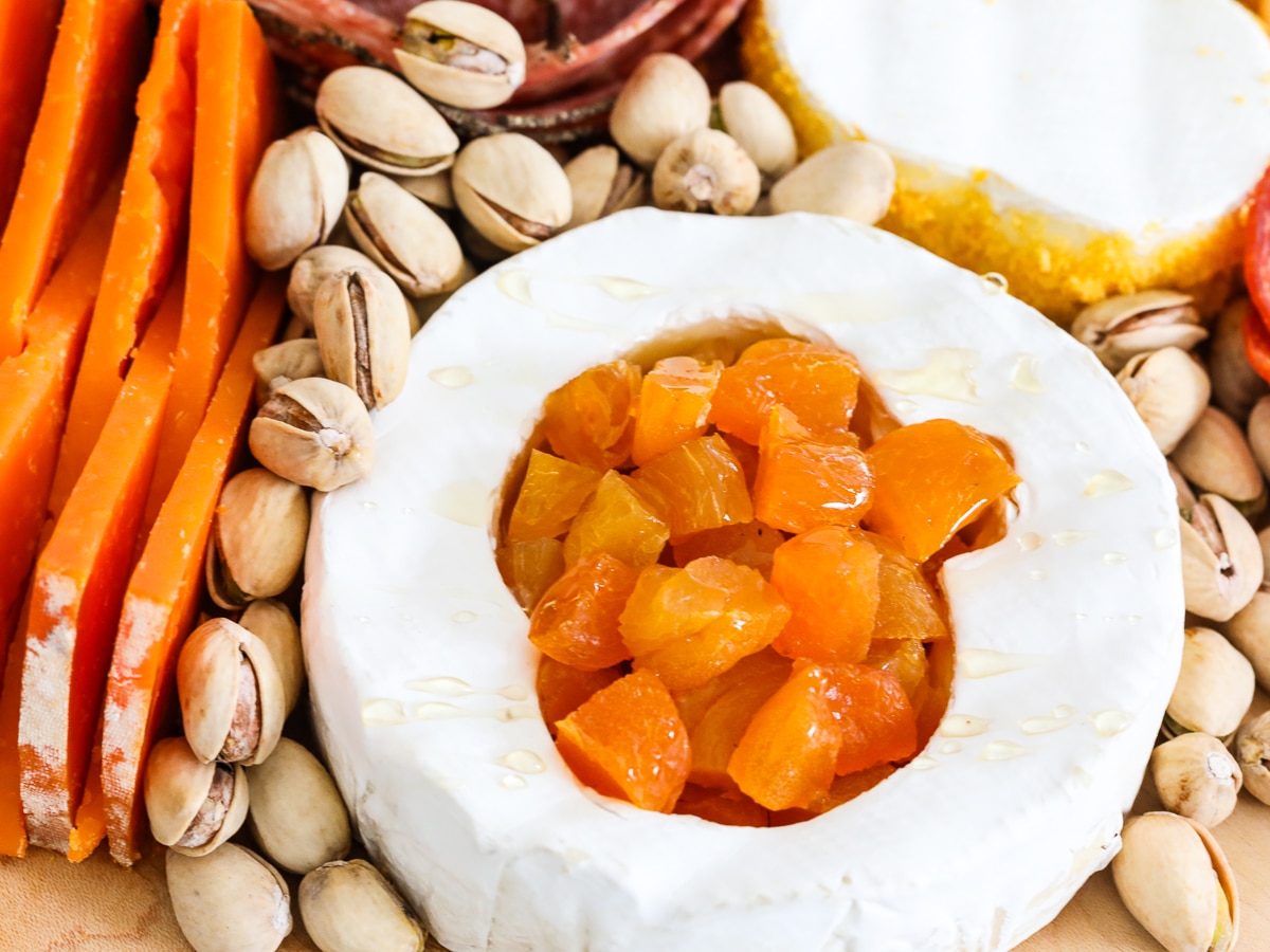A round brie with pumpkin shape cut out filled with chopped apricots and surrounded with pistachios.