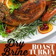 A golden brown roast turkey with a seasoning rub on a white platter garnished with oranges and herbs.
