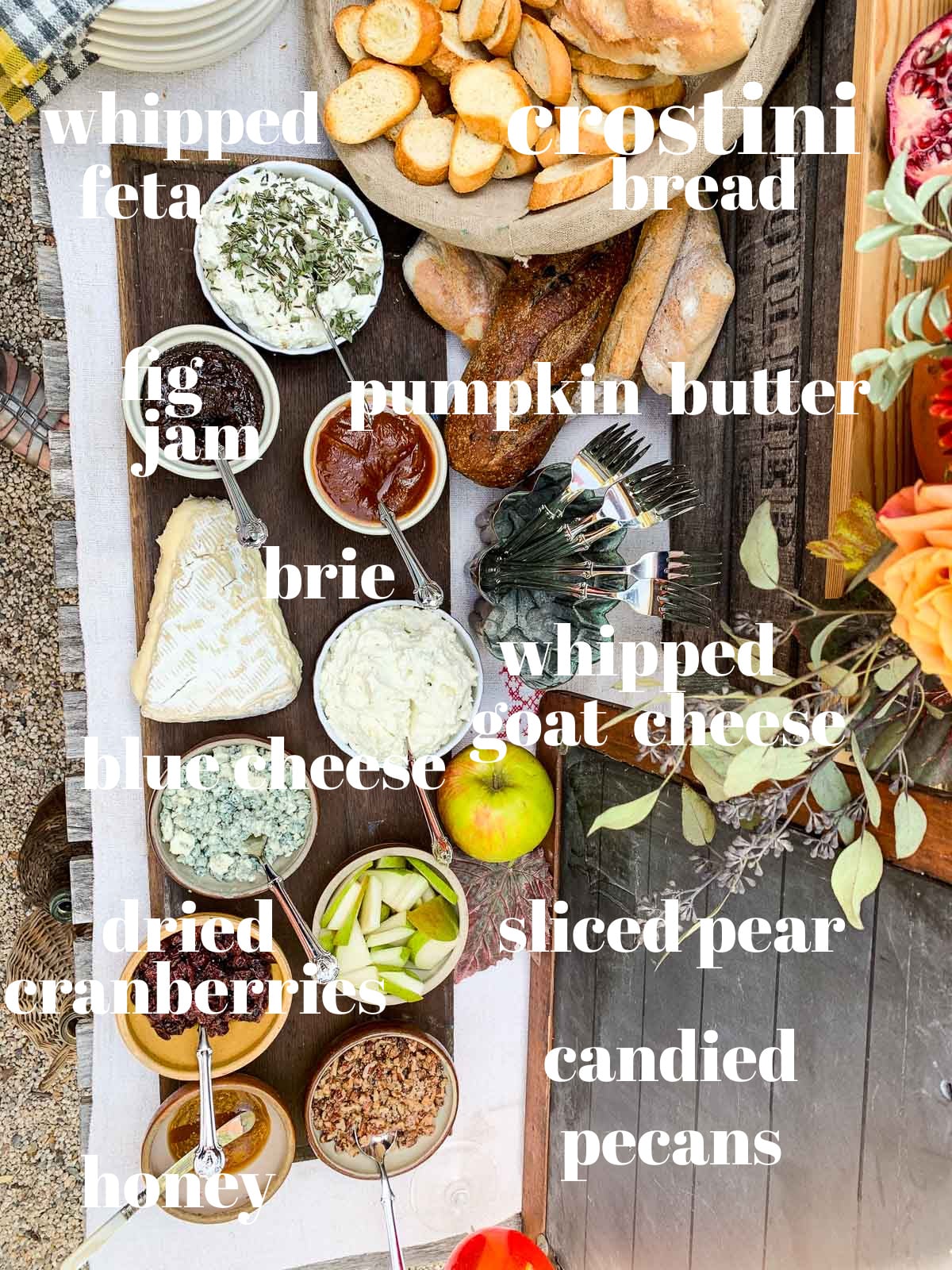 A rustic table with crostini and toppings labled for an outdoor Fall party. 