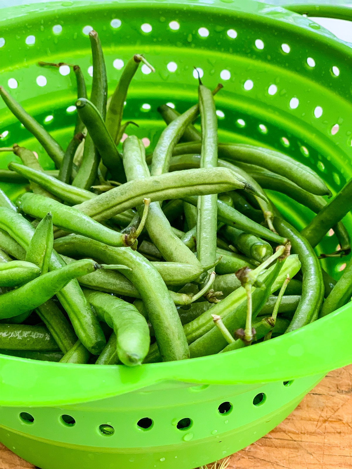 A green colander full of fresh green beans. 