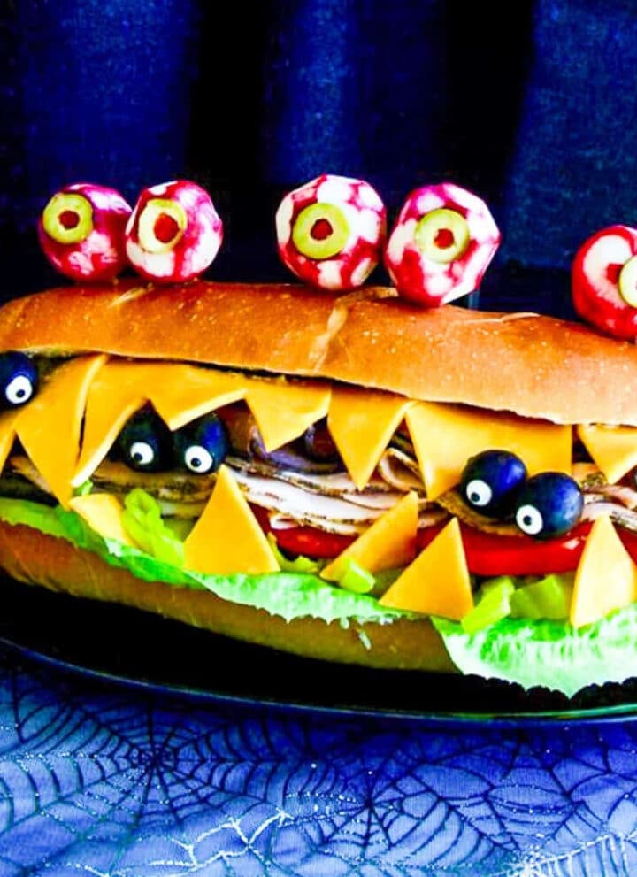 A giant sub sandwich that looks like a Monster with giant edible radish eyes and small black olive eyes.