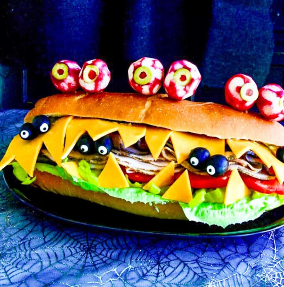 A giant sub sandwich that looks like a Monster with giant edible radish eyes and small black olive eyes.