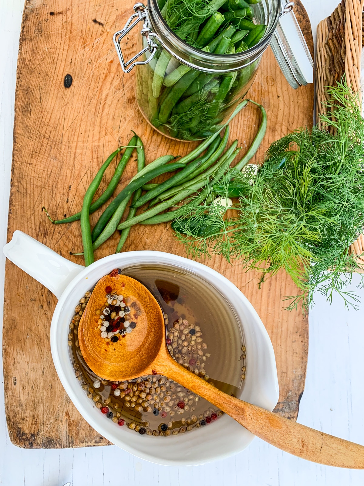 A cutting board with all the ingredients to make green bean pickles. 