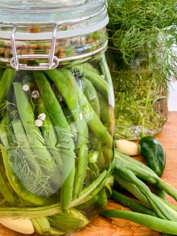 A clear glass jar filled with pickled green beans on a cutting board.