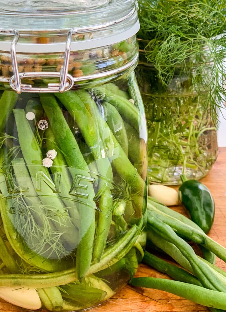 A clear glass jar filled with pickled green beans on a cutting board.