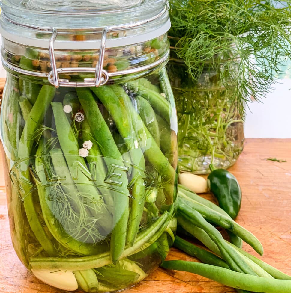 A clear glass jar filled with pickled green beans on a cutting board.