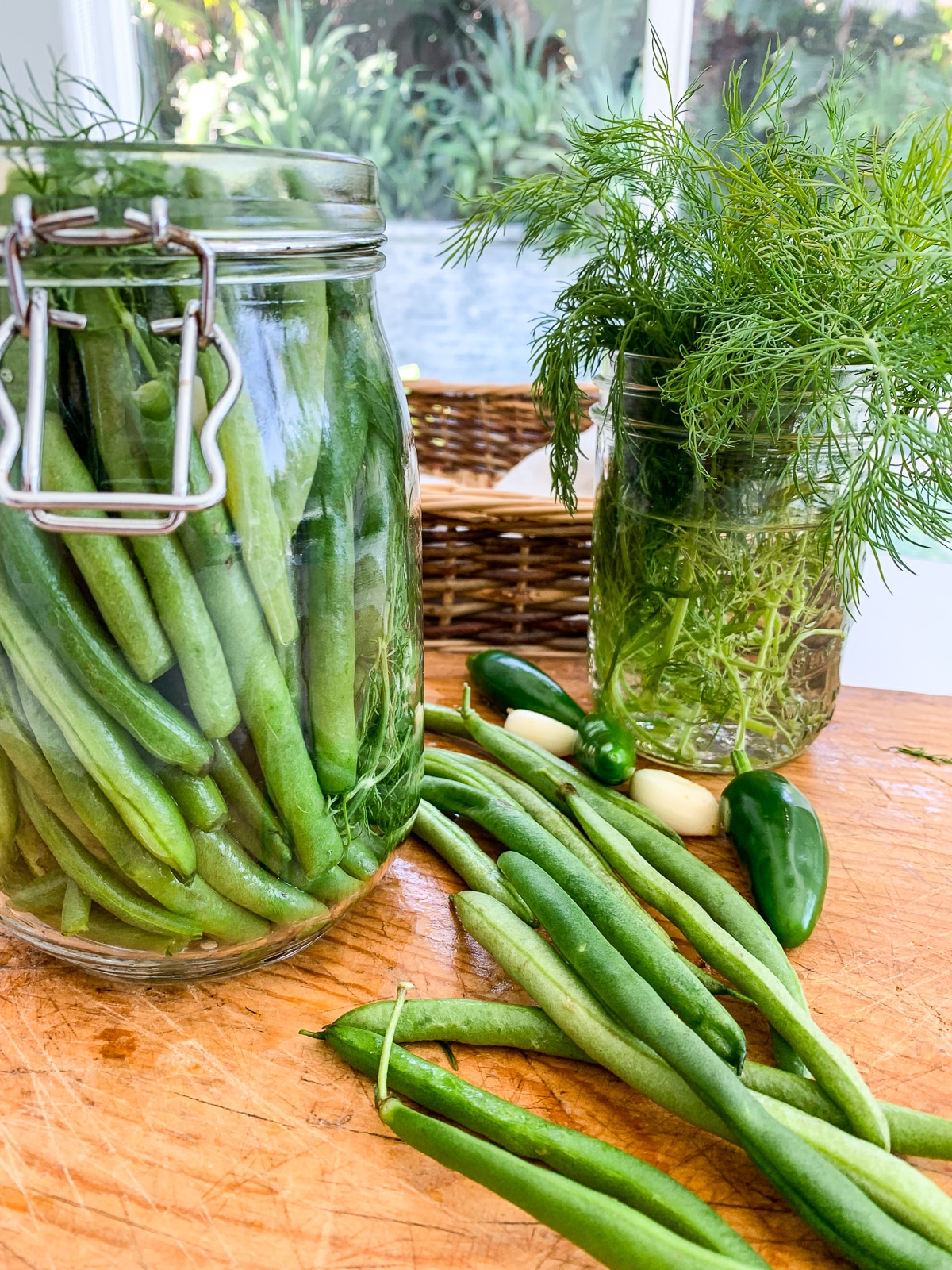 A clear clamp jar filled with pickled green beans and ingredients on a cutting board.