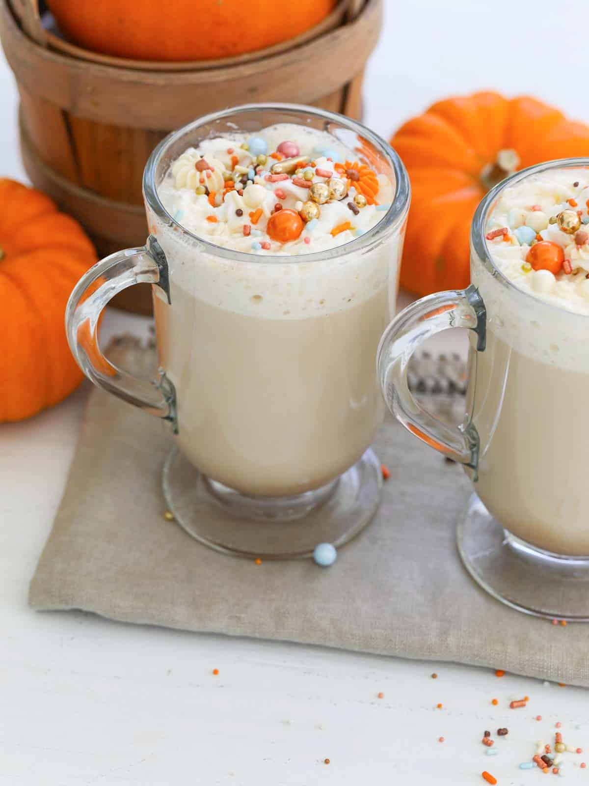 Two mugs of Pumpkin Spice Latte with Fall sprinkles on top of whip cream.