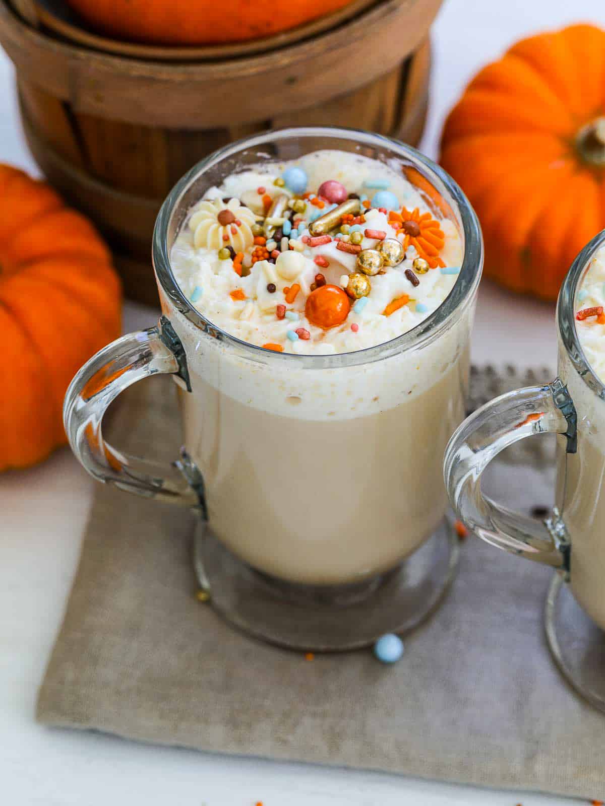 2 pumpkin latte coffee drinks on a table with mini pumpkins.