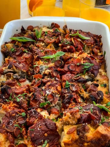 Lifting out a piece of breakfast casserole from a white baking dish with a serving utensil from the strata.