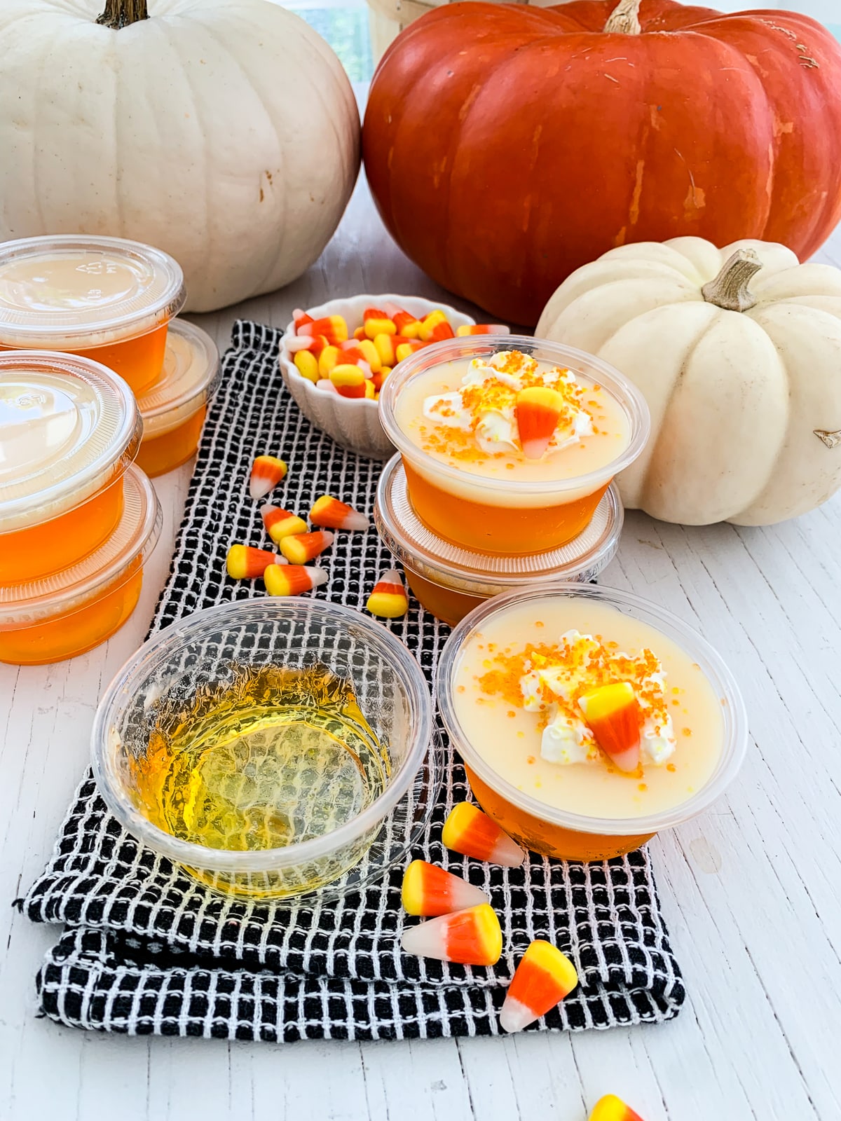 A candy corn Jello shot cup that is empty with just a bit of yellow Jello and other cups full some garnished with whipped cream and candy corn. 