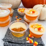 Close up of a candy corn Jello shot that is half sipped and others in plastic cups at a party with candy corn in the background.