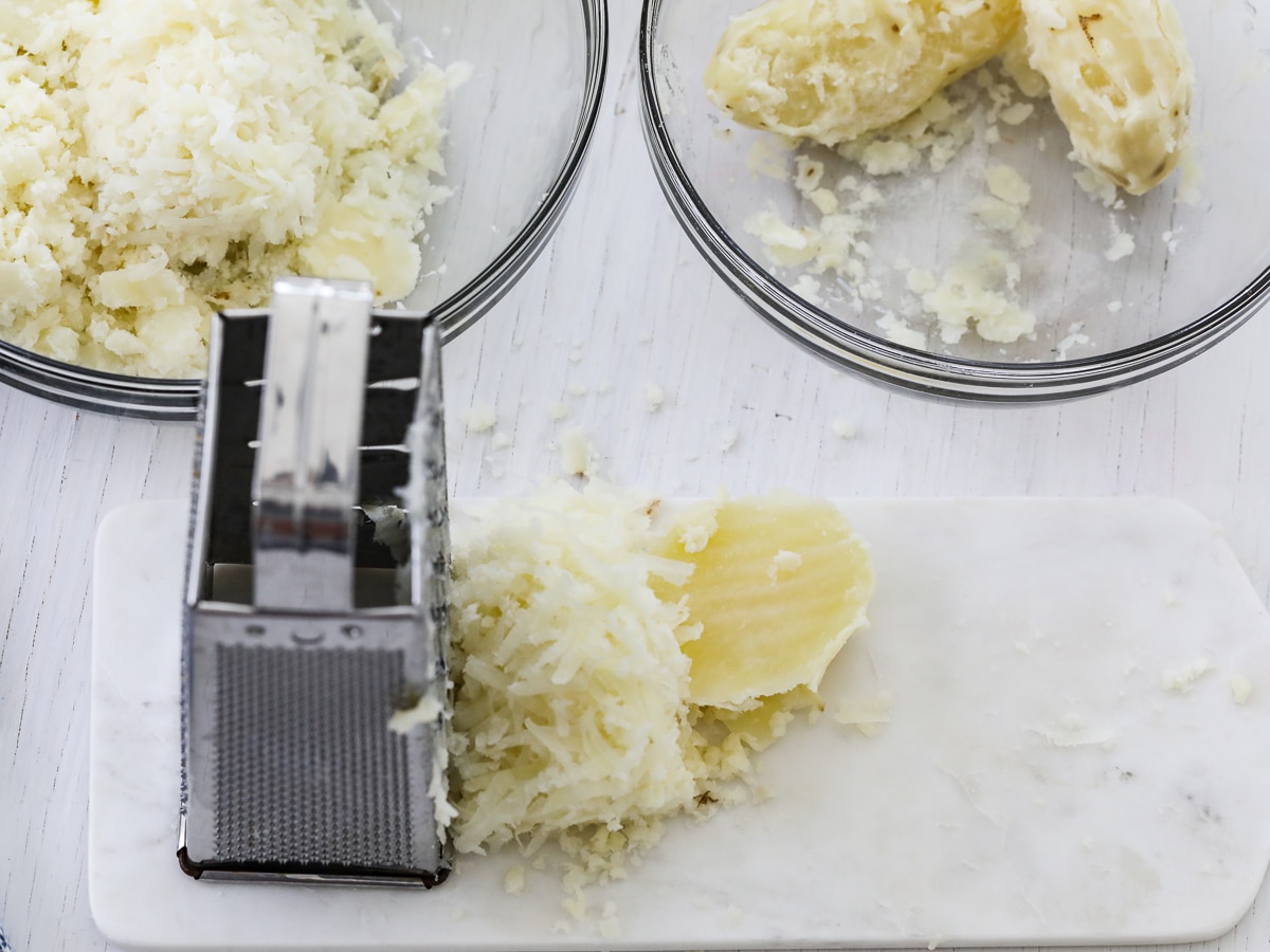 Grating cooked potatoes on a hand box grater to make a potato casserole. 