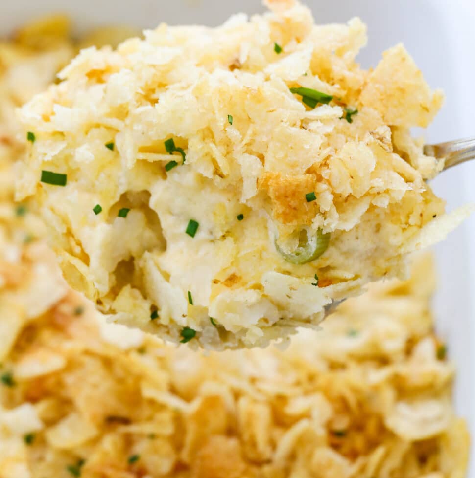 A large spoon holding a scoop of hot potato casserole serving it for dinner.