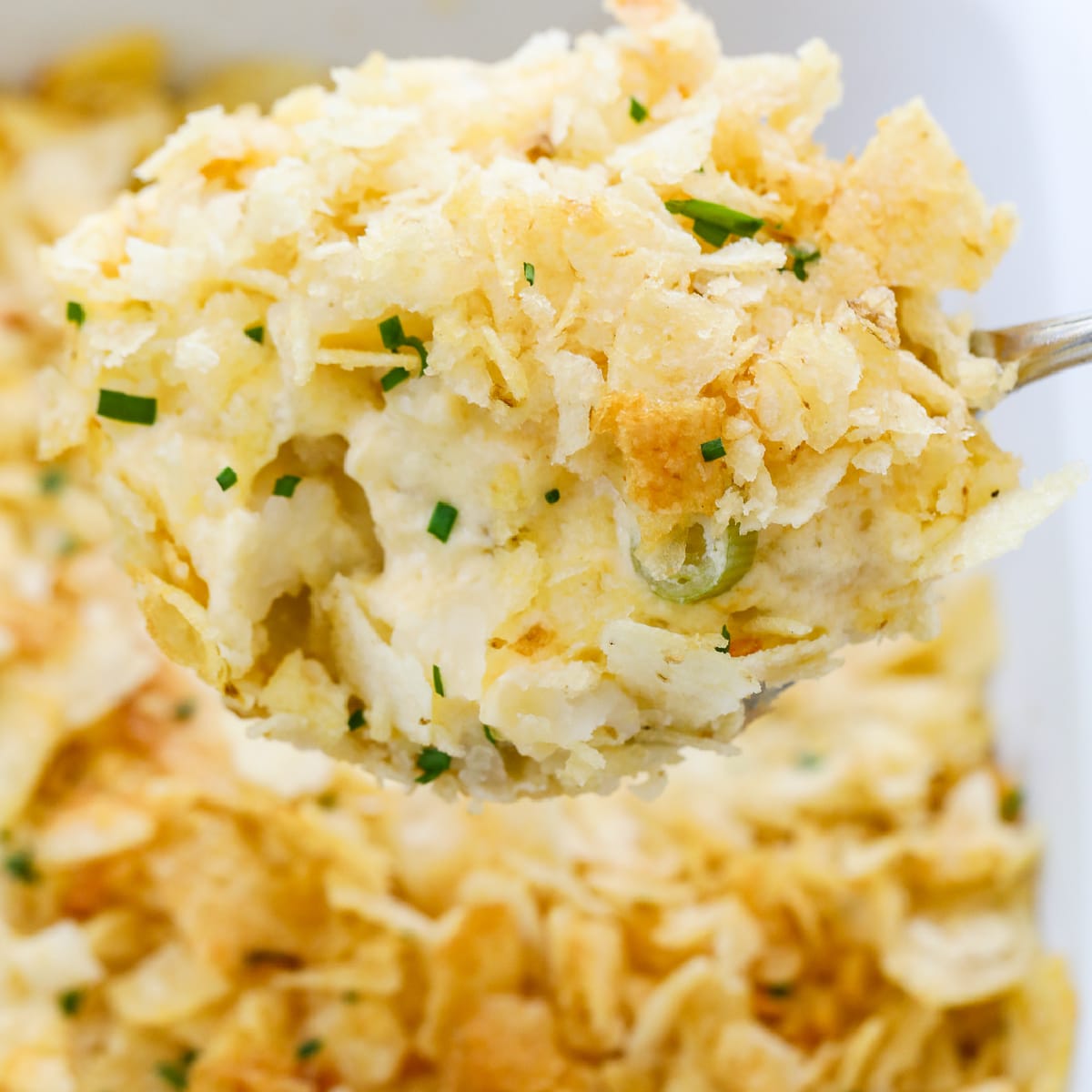 A large spoon holding a scoop of hot potato casserole serving it for dinner.