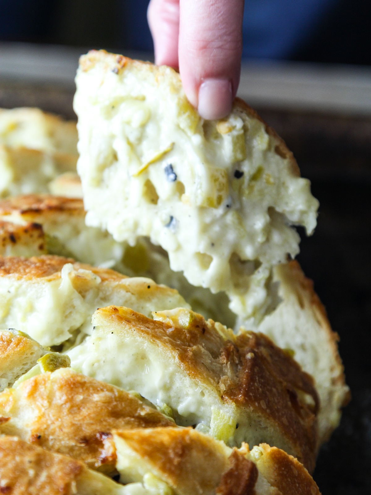 A lady pulling a piece of cheesy pull apart bread from a loaf of crack bread. 