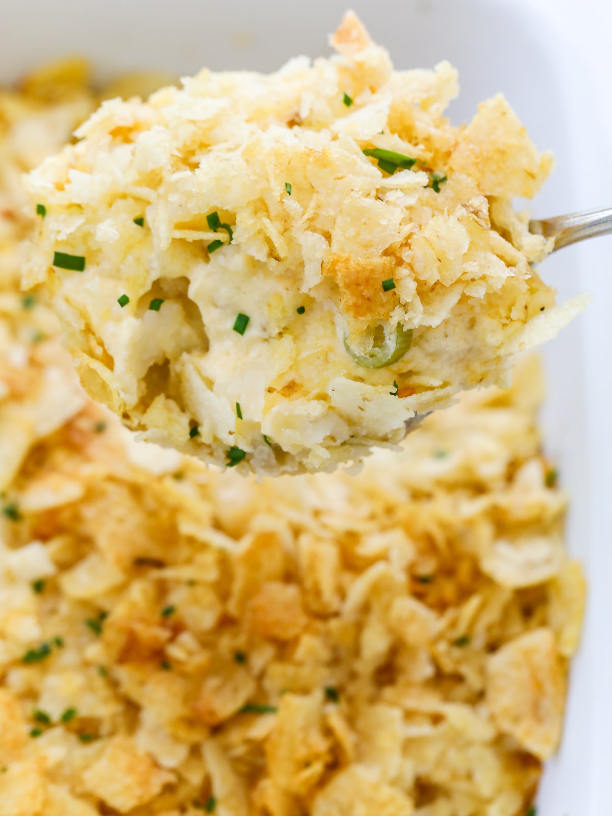 A large spoon holding a scoop of hot potato casserole serving it for dinner. 