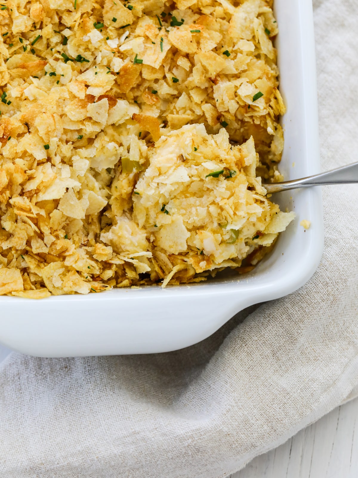 Scooping out a serving of potato casserole from a white baking dish. 