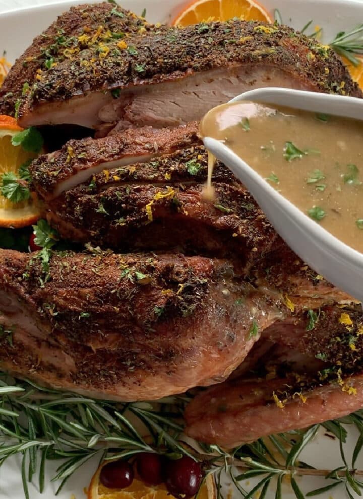 A dark golden roast turkey with a white gravy boat pouring turkey gravy on top.