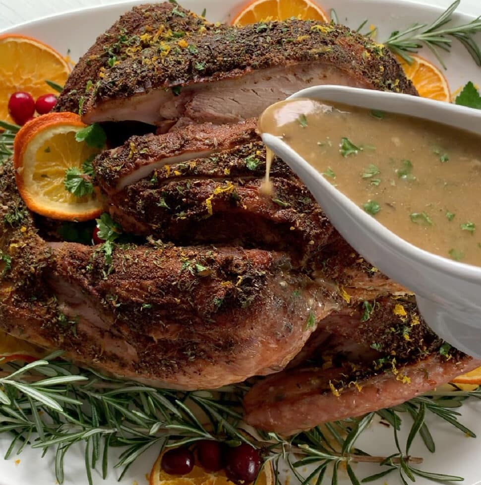 A dark golden roast turkey with a white gravy boat pouring turkey gravy on top.