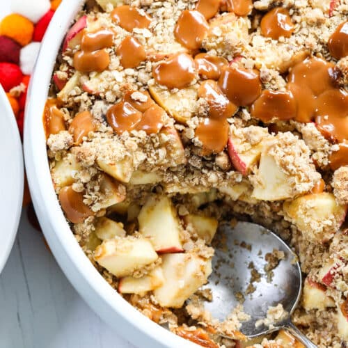 A round white dish of fresh baked caramel apple crisp with a large serving spoon for a Fall dessert.