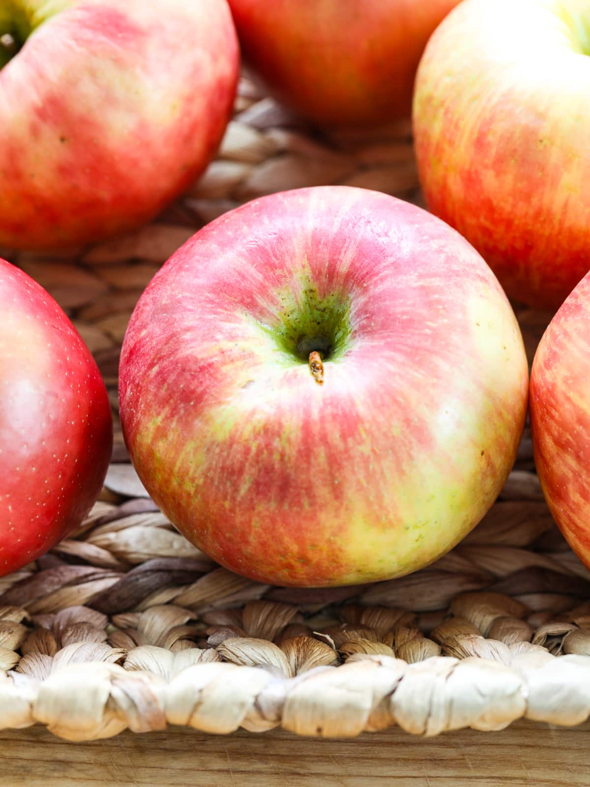 A honeycrisp apple in a ratan basket up close, with bright pink and yellow colors.