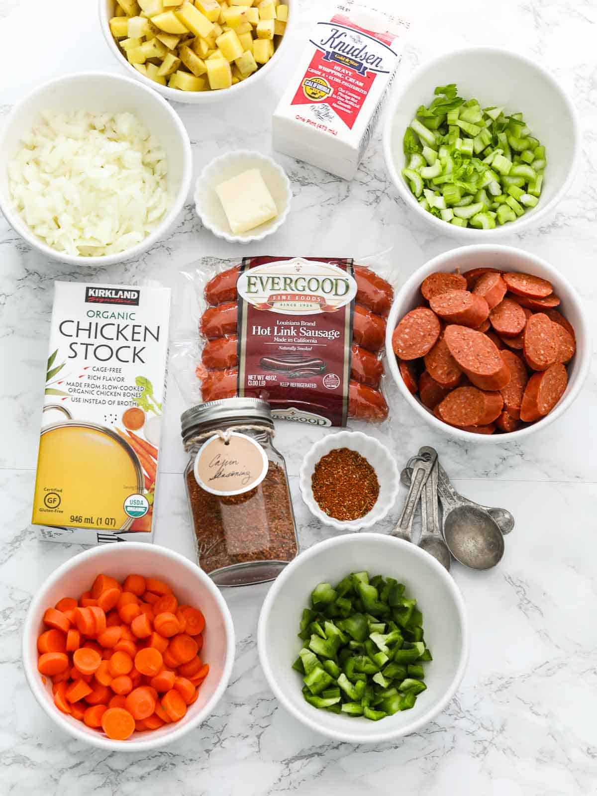 Ingredients on a marble table to make a Cajun sausage potato soup in a crock pot.
