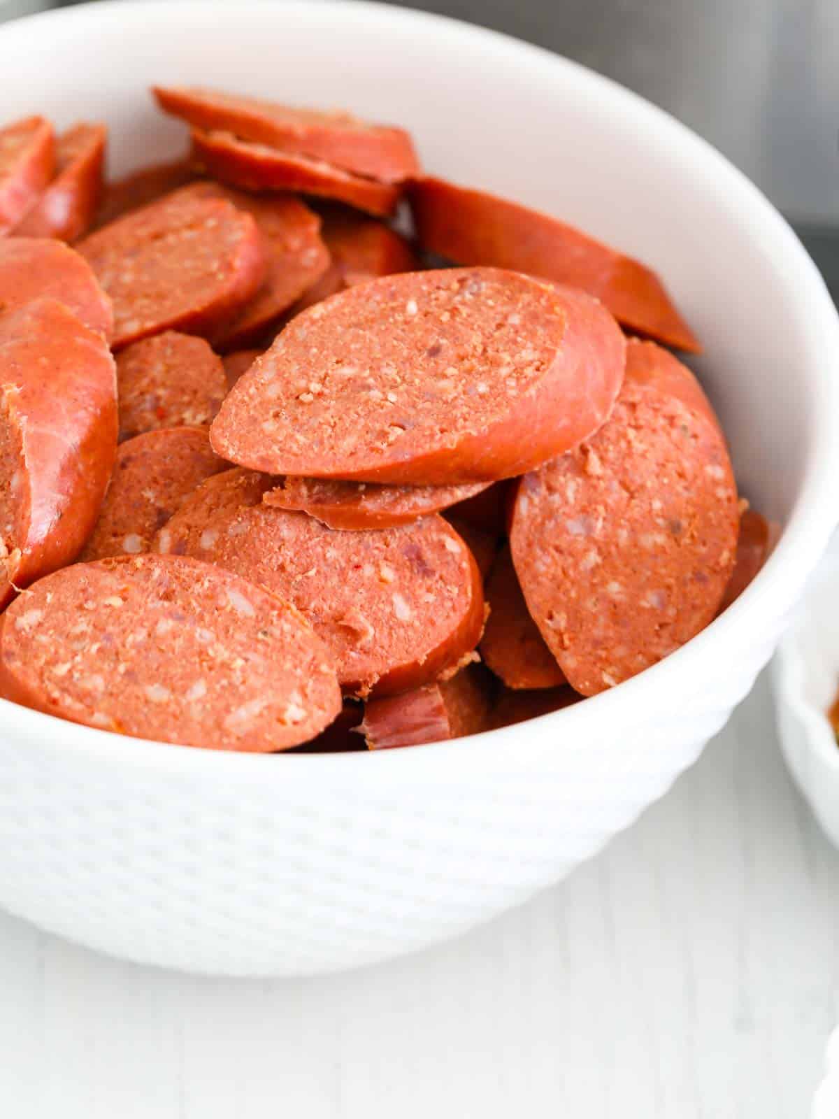 Thin slices of Cajun andouille sausage in a white bowl to use in a recipe for soup.