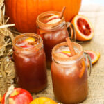 Apple cider Fall sangria in glasses next to a real pumpkin with fruit and garnished with cinnamon sticks.