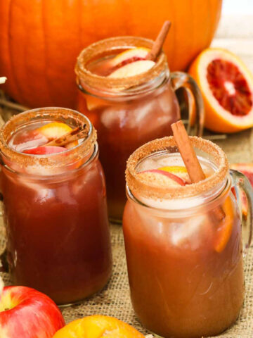 Apple cider Fall sangria in glasses next to a real pumpkin with fruit and garnished with cinnamon sticks.