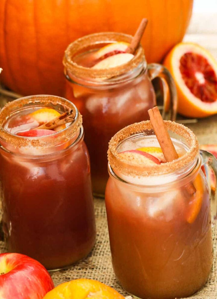 Apple cider Fall sangria in glasses next to a real pumpkin with fruit and garnished with cinnamon sticks.
