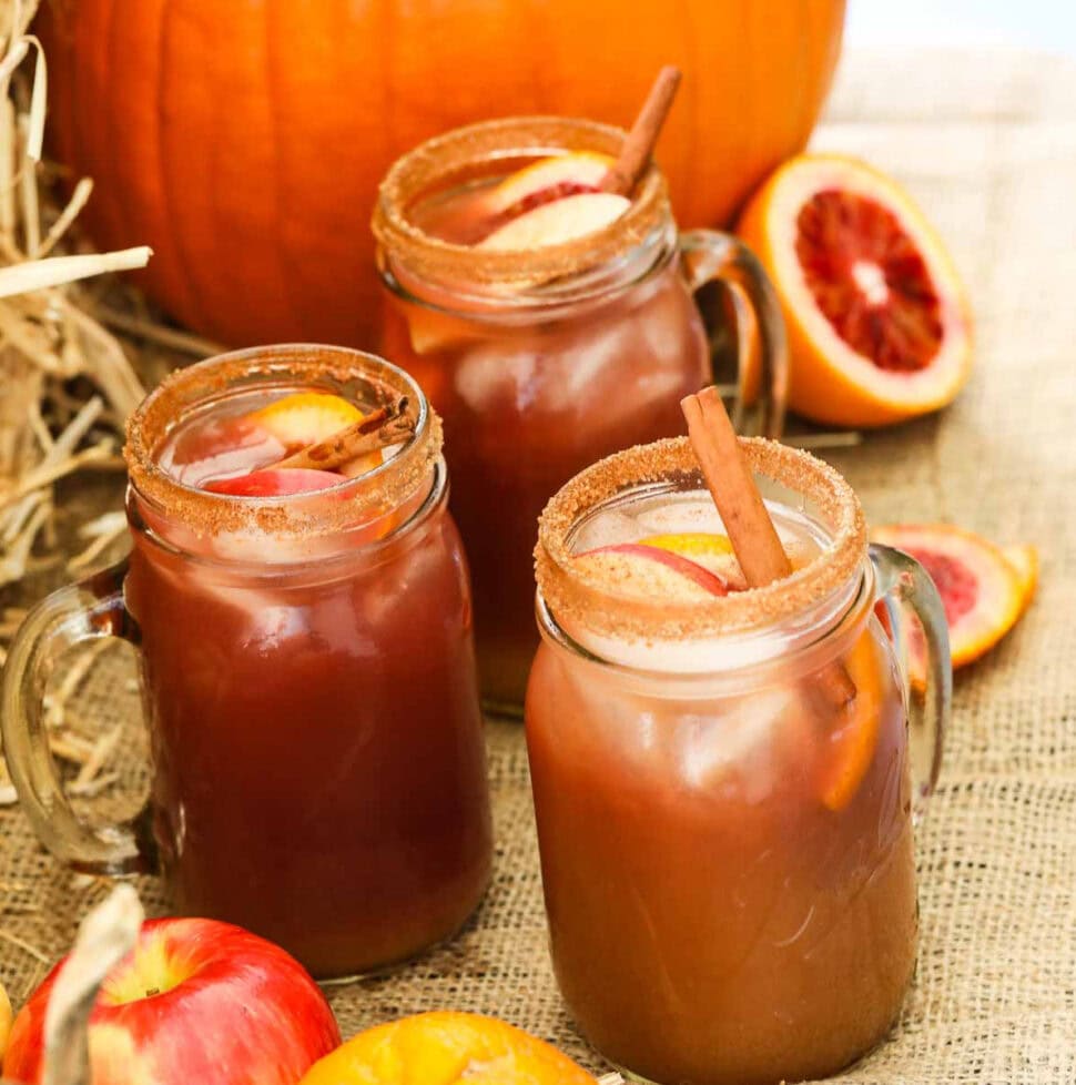 Apple cider Fall sangria in glasses next to a real pumpkin with fruit and garnished with cinnamon sticks.